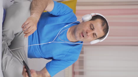 Vertical-video-of-Man-listening-to-music-with-headphones-is-unhappy-and-sad.